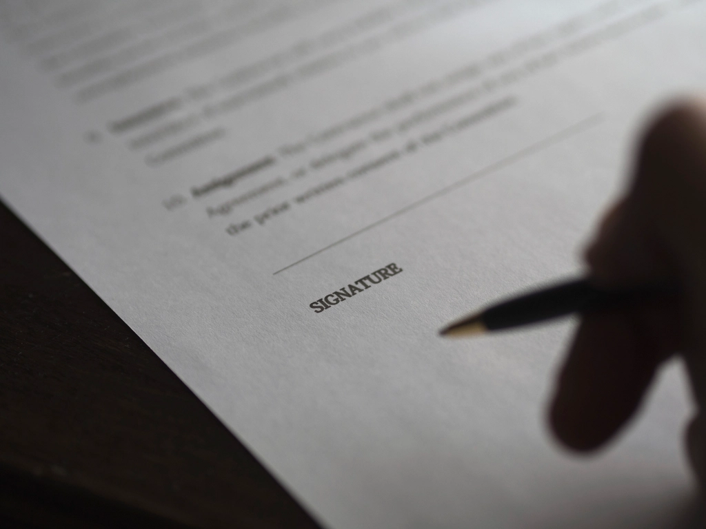 Close-up of a hand holding a pen over a contract before signing